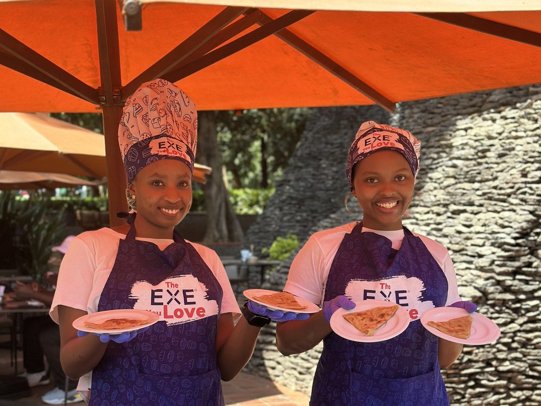 Two hostesses in branded aprons presenting plated food at an outdoor stand