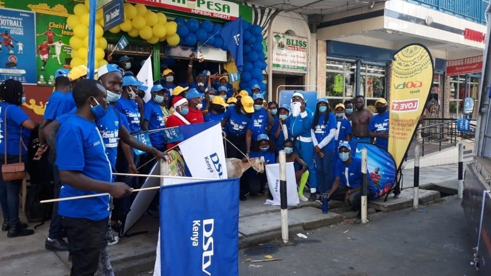 A street team in blue carrying branded flags along a road
