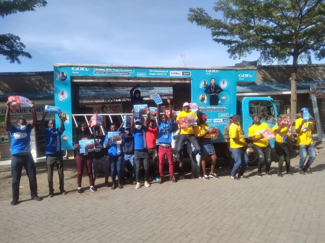 A large team lined up in front of a branded mobile stand