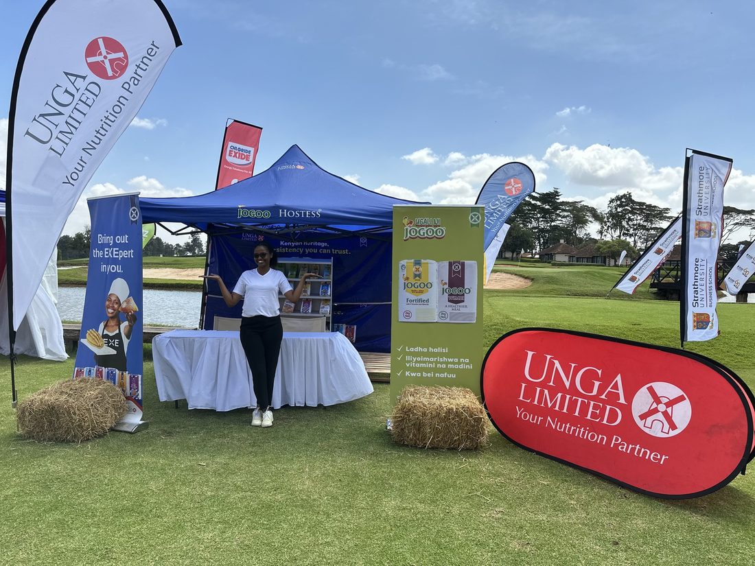 A host in uniform working an Unga Limited stand set on a lawn with hay bales and branded flags