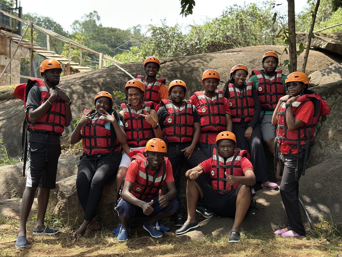A rafting crew in helmets and buoyancy aids grouped together on the rocks at the river edge