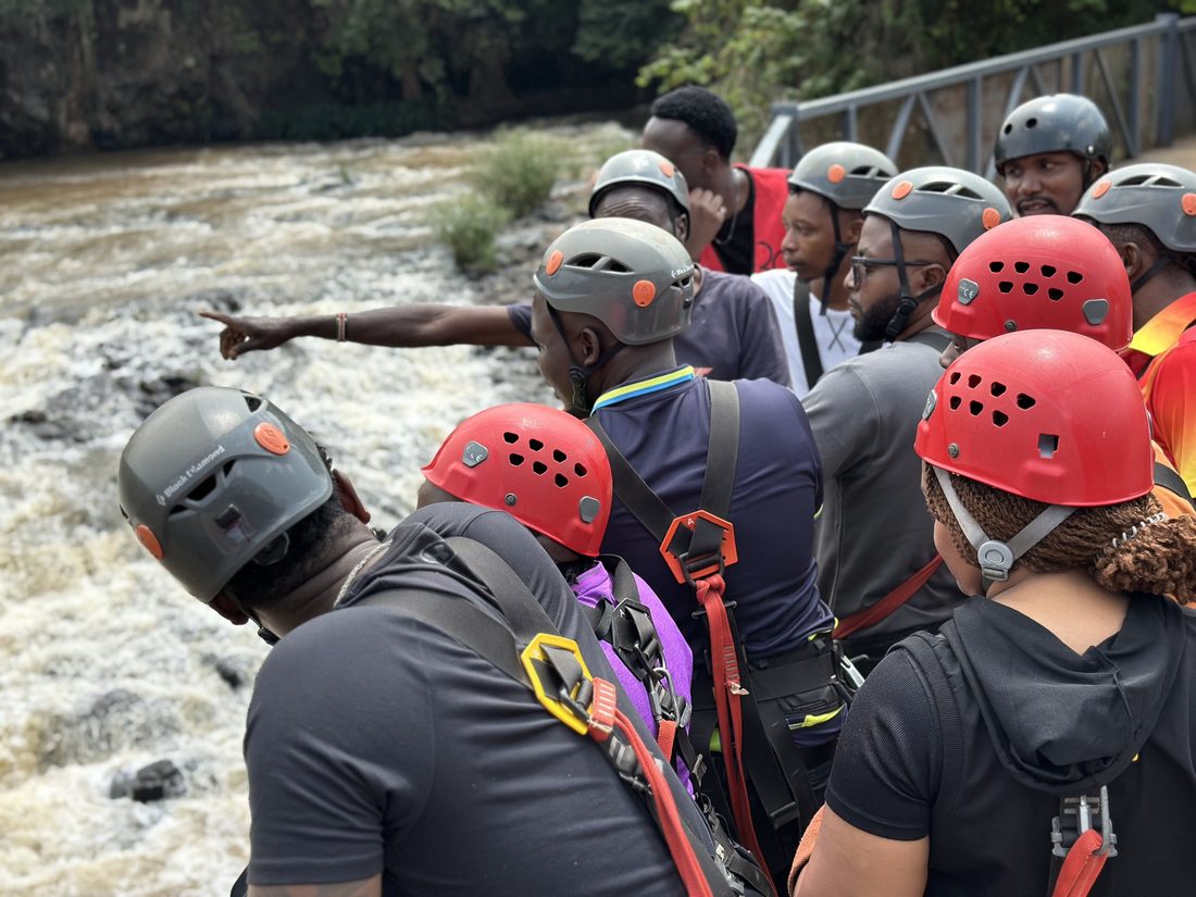 A group in helmets and safety gear being briefed at the water’s edge