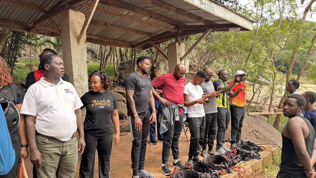 A group standing in a line under a shade structure at an outdoor activity venue with kit laid out in front of them