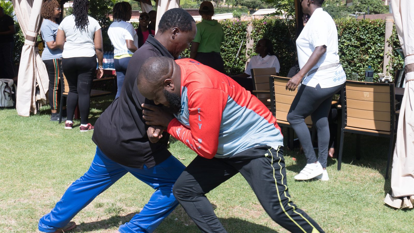 Two people straining against each other in a tug of war on a lawn while colleagues watch