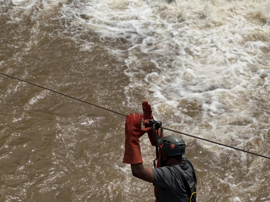 A person crossing a river on a zip line above fast water