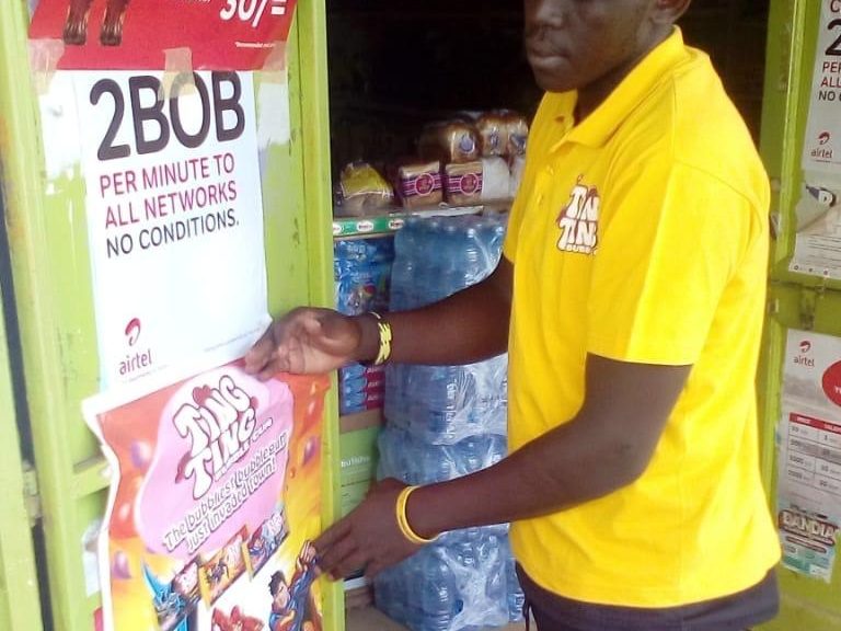 A field representative in a branded polo fixing a point-of-sale poster to a shop door