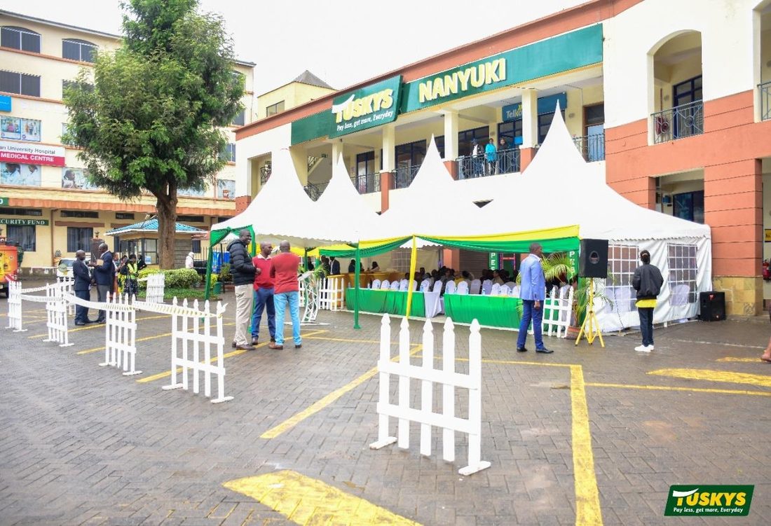 Twin marquees and seated guests in the car park of a Tuskys Nanyuki store