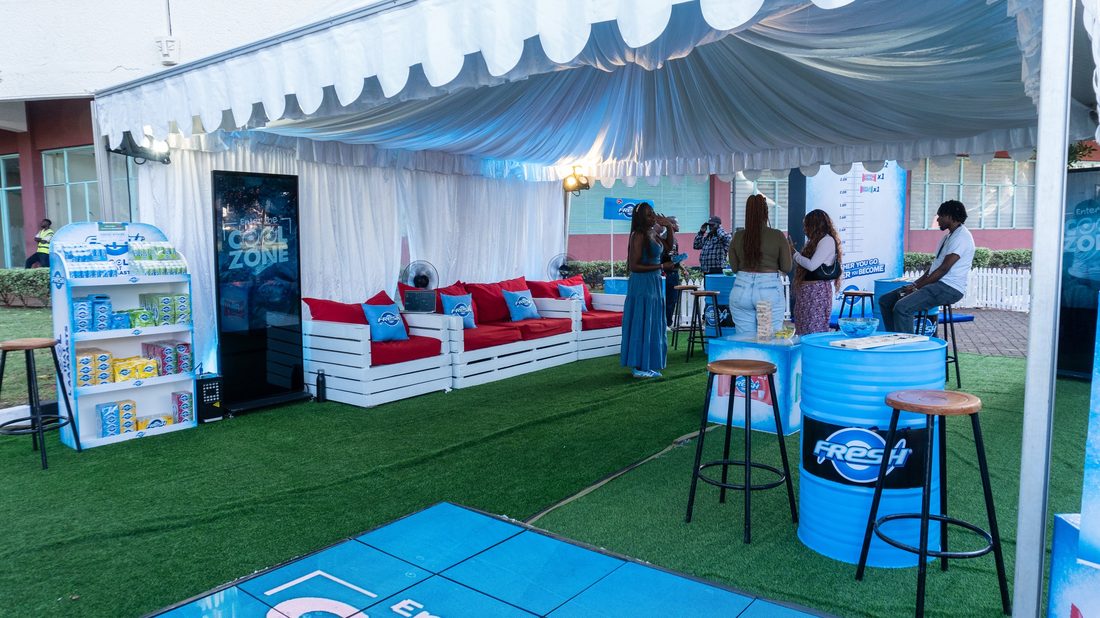 A branded lounge built on artificial turf with blue banquette seating and a stocked display unit