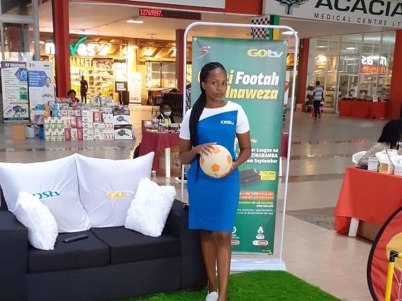 A lounge set on artificial turf inside a shopping centre with a host alongside